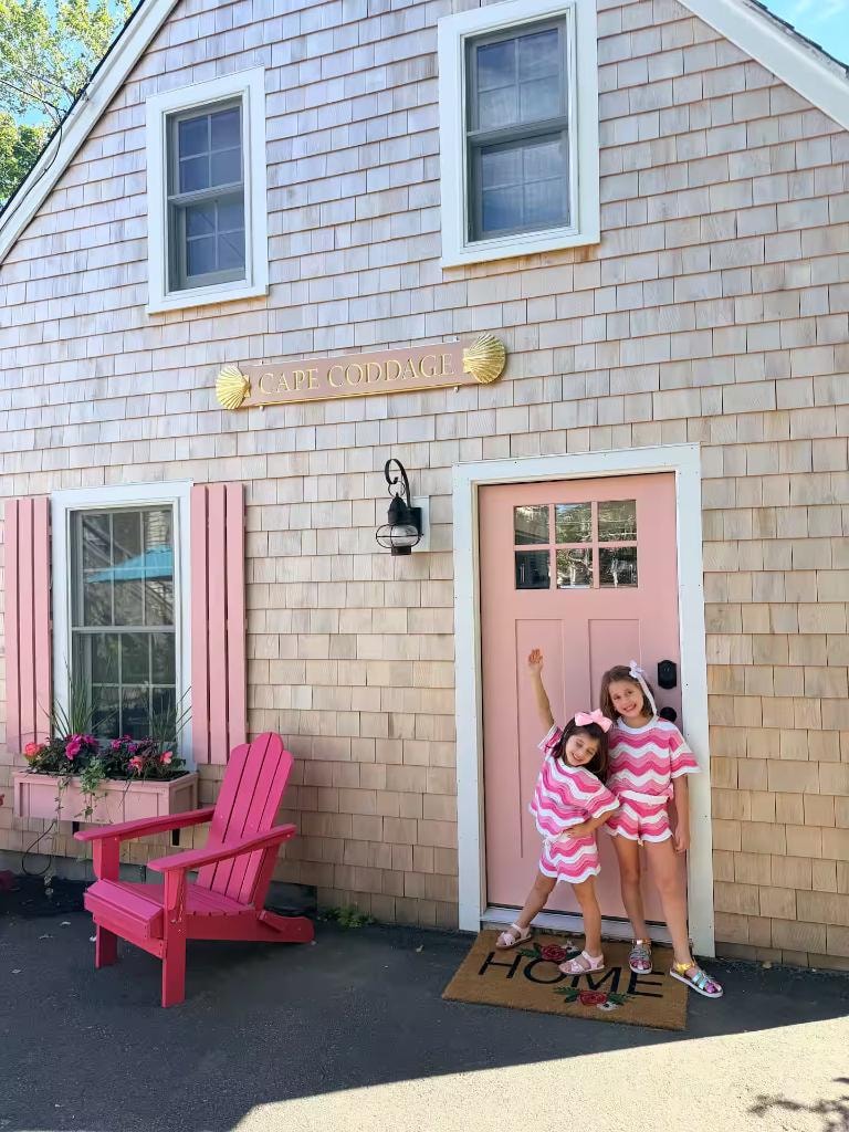 Two young guests in matching outfits posing at the Cape Coddage pink front door